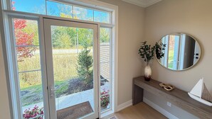 Ein Zimmer mit einer Schiebetür, die zu einem Garten führt, einem runden Spiegel an der Wand und einer Bank mit Blumen in einer Vase.