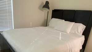 En säng med en vit madrass och kuddar, en mörk sänggavel och en golvlampa.