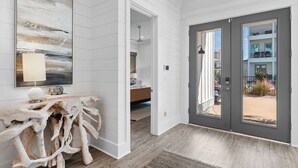 A modern interior with a wooden console table, a large abstract painting, and a view through a grey door to an outdoor area. - 6 Bedrooms | 6.5 Bathrooms | Sleeps 22 (Miramar Beach)