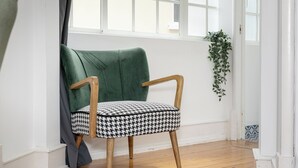 A chair with wooden legs and a houndstooth cushion, positioned near a window with a view of the outside.