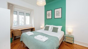 A bedroom with a bed, a desk, a chair, a window, and two wall-mounted lamps.
