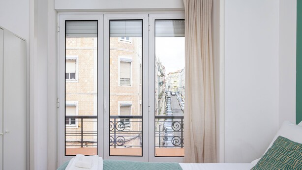 A bedroom with a bed, a window with a view of buildings, and a curtain.