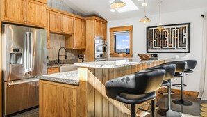 Eine moderne Küche mit Holzausstattung, Edelstahlgeräten, einer Granit Arbeitsplatte und einer Bar mit Hockern.