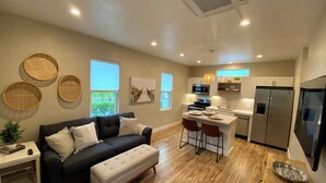 A modern kitchen with a central island, a dining area with two chairs, a black sofa, and a small side table with a plant.