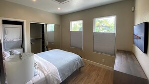 A bedroom with a bed, a walk-in closet, a window with blinds, and a ceiling vent.