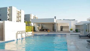 A modern pool area with a clear blue pool, surrounded by white buildings and a covered seating area. - Caribbean home / Punta Cana /Pool, gym, playground area (Punta Cana)