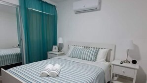 A hotel room with a bed, a nightstand, a lamp, a mirror, and a window with curtains. - Caribbean home / Punta Cana /Pool, gym, playground area (Punta Cana)