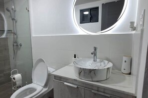 A modern bathroom with a round mirror, a marble sink, and a toilet.