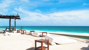 A beachside lounge with white cushioned seating and wooden tables, overlooking the ocean. - Ocean View Suite 2 Cancun (Cancún)