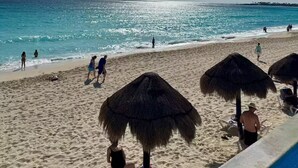A beach with thatched umbrellas, a clear sky, and calm sea. - Ocean View Suite 2 Cancun (Cancún)