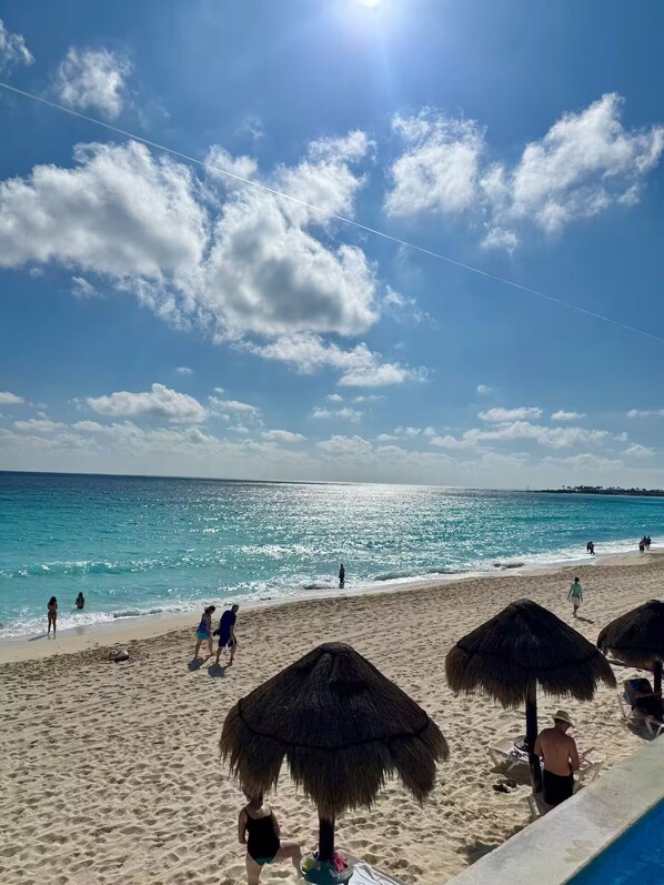 A beach with thatched umbrellas, a clear sky, and calm sea. - Beautiful Caribbean Spectacular Ocean View (Cancún)