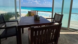 A beachside dining area with a table and chairs, large windows offering a view of the ocean and beach. - Ocean View Suite 2 Cancun (Cancún)