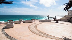 A sunlit outdoor lounge area with a curved seating arrangement, a small table, and a view of the ocean. - Beautiful Caribbean Spectacular Ocean View (Cancún)