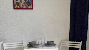 A small white table with two chairs, a colorful painting on the wall, and a dark curtain. - Beautiful Caribbean Spectacular Ocean View (Cancún)