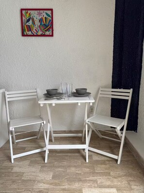 A small white table with two chairs, a colorful painting on the wall, and a dark curtain. - Beautiful Caribbean Spectacular Ocean View (Cancún)