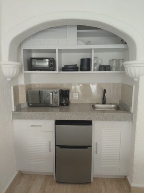 Una cocina compacta con armarios blancos, microondas, cafetera y lavavajillas.