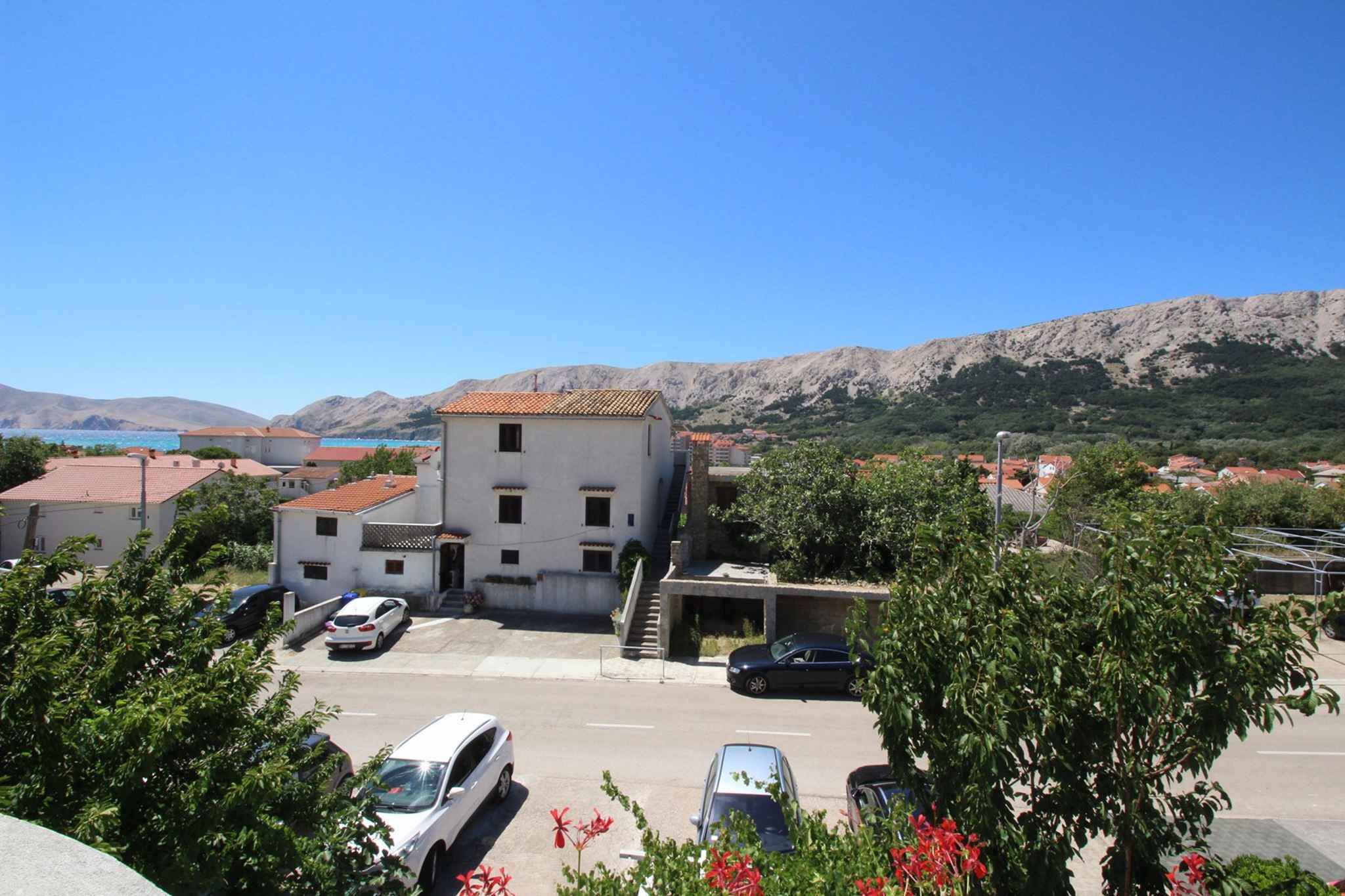 A building with a red-tiled roof, a parking area with several cars, and a mountainous backdrop.