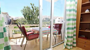 Ein Balkon mit Tisch und Stühlen, einem Holzschrank und Blick auf Gebäude und Hügel.