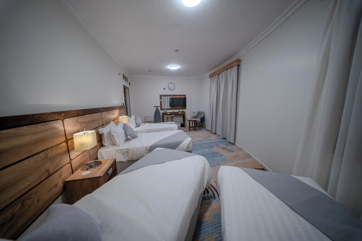 Une chambre d’hôtel avec trois lits simples, un bureau avec une chaise, une télévision et une horloge murale.