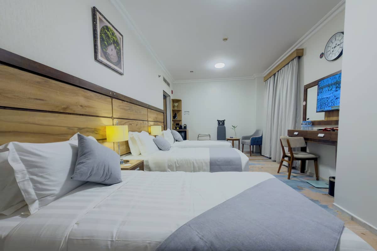 Une chambre d’hôtel avec deux lits, un bureau, une chaise, une horloge et un téléviseur.