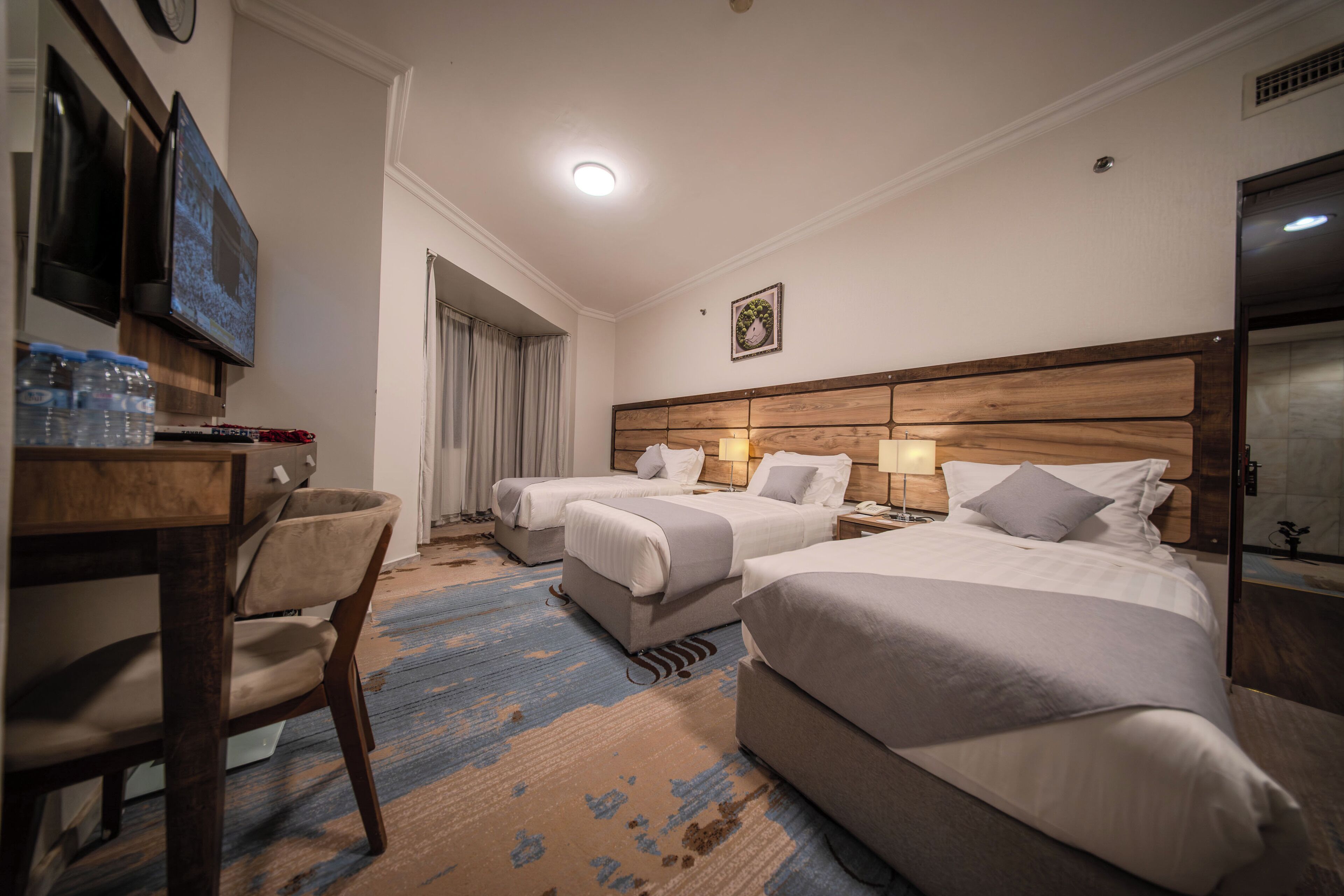 A hotel room with two beds, a desk with a chair, a television, and a clock on the wall.