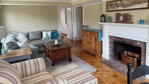 Ein Wohnzimmer mit einer Couch, einem Streifenstuhl, einem Holztisch, einem Kamin und einer Küchenzeile mit Schränken und einer Arbeitsfläche.