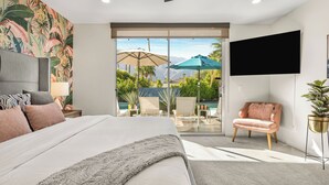 Habitación de hotel con cama, televisión, una silla y vistas a una piscina y montañas.