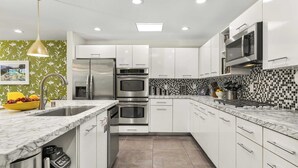 Una cocina moderna con armarios blancos, electrodomésticos de acero inoxidable, una encimera de mármol y un salpicadero a cuadros.