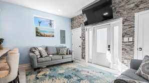 A modern living room with a grey sofa, a blue and beige rug, and a stone wall. - Pensacola Retreat w/ Jacuzzi Tub, Outdoor Lounge & Fire Pit Historic Church 1928 by Avantstay (Pensacola)