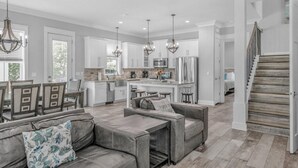 A spacious living area with a gray sofa, a dining table with chairs, and a kitchen in the background.