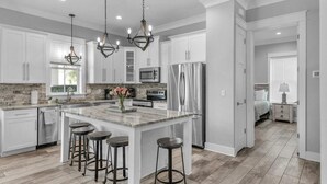 A modern kitchen with white cabinets, a large island with stools, stainless steel appliances, and pendant lighting.