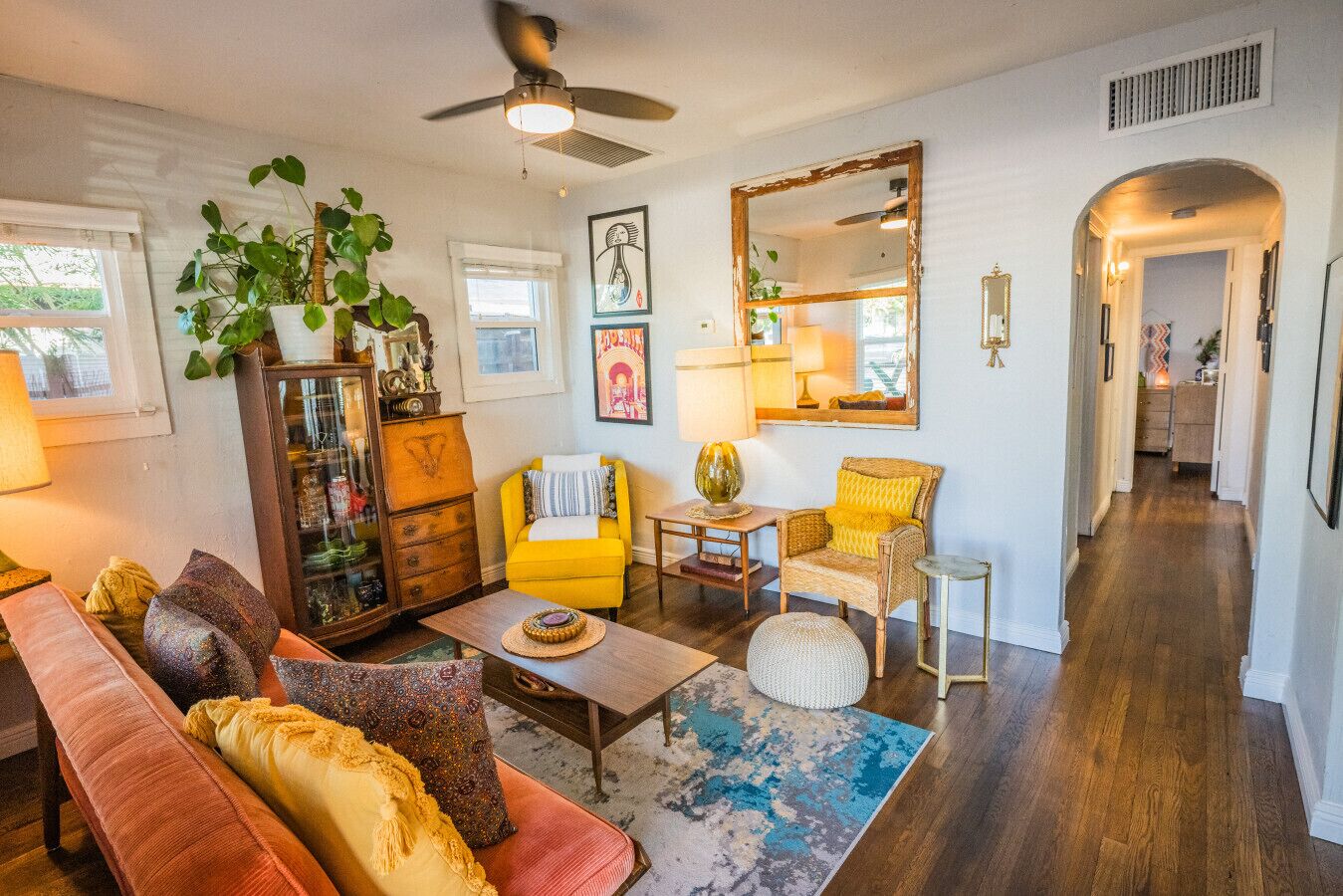 A cozy living room with a sofa, armchair, and coffee table, a bookshelf, and a large mirror.