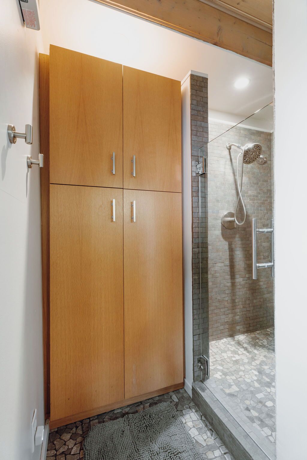 A bathroom with a wooden wardrobe, a shower with a glass door, and a tiled floor.