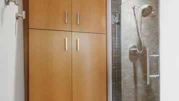 A bathroom with a wooden wardrobe, a shower with a glass door, and a tiled floor.