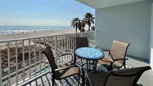 Ein Balkon mit Blick auf den Strand, einem Tisch und zwei Stühlen.