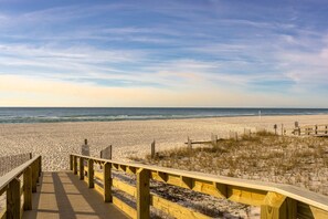 A wooden boardwalk leading to a beach with dunes and a clear sky.