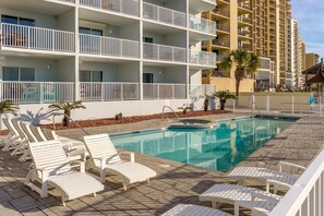 A hotel with a swimming pool, white lounge chairs, and a multi-story building with balconies.