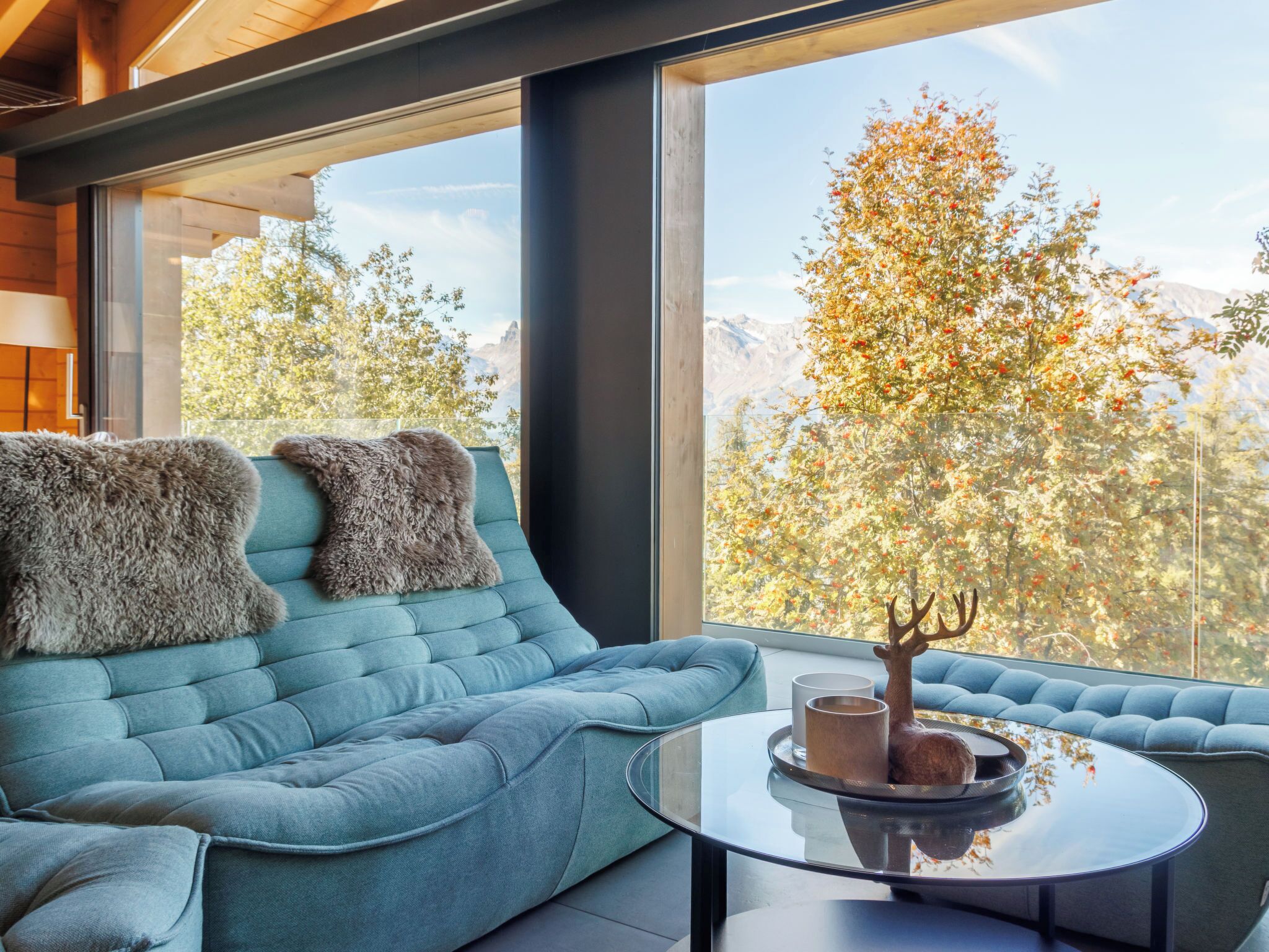 Ein modernes Wohnzimmer mit einem blauen Sofa, zwei flauschigen Zierkissen und einem Glastisch mit einer dekorativen Hirschskulptur.