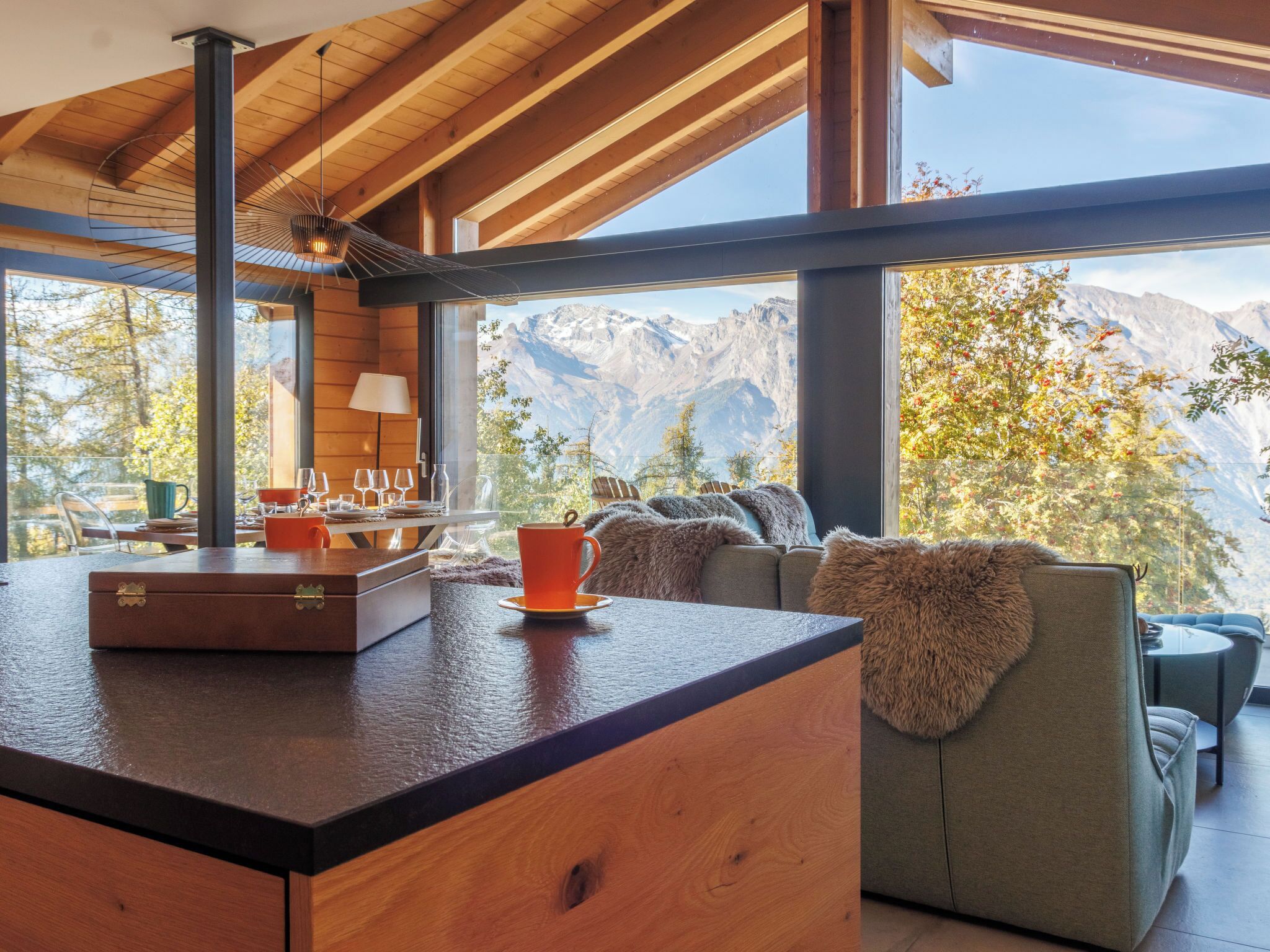 Eine moderne Küche mit Holzarbeitsplatte, eine Essecke mit Tisch und Stühlen und ein Blick auf Berge durch große Fenster.
