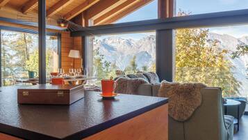 Eine moderne Küche mit Holzarbeitsplatte, eine Essecke mit Tisch und Stühlen und ein Blick auf Berge durch große Fenster.