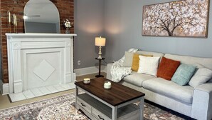 A living room with a fireplace, a sofa, a coffee table, and a painting on the wall. - Newly renovated 2 bedroom home located near the waterfront and Carnegie Library! (Munhall)