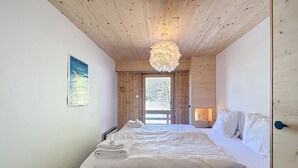 Un dormitorio con techo de madera, una cama con ropa blanca, un cartel en la pared y una ventana con vistas a la vegetación.