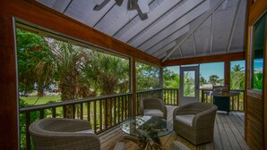 Uma área externa coberta com móveis de vime, uma mesa de vidro e vista para o exterior.
