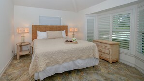 Quarto com cama, mesas de cabeceira, cômoda e janela com persianas.