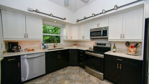 Uma cozinha moderna com armários brancos e pretos, eletrodomésticos de aço inoxidável e piso de ladrilho de pedra.