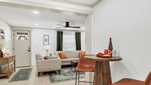 Un salon comprenant un canapé, des fauteuils, une table basse et une table à manger avec une bouteille et des fruits.