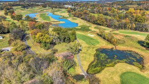 Vue aérienne d’un terrain de golf avec plusieurs étangs, des routes sinueuses et des zones boisées environnantes.