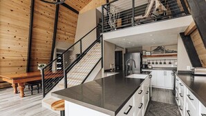 A modern kitchen with a central island, white cabinetry, and a staircase leading to an upper level.