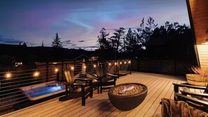 A wooden deck with a hot tub, outdoor seating, and string lights.