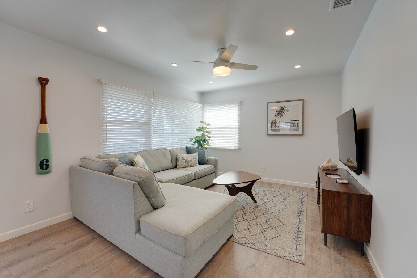 A living room with a sectional sofa, a coffee table, a TV, and a ceiling fan.
